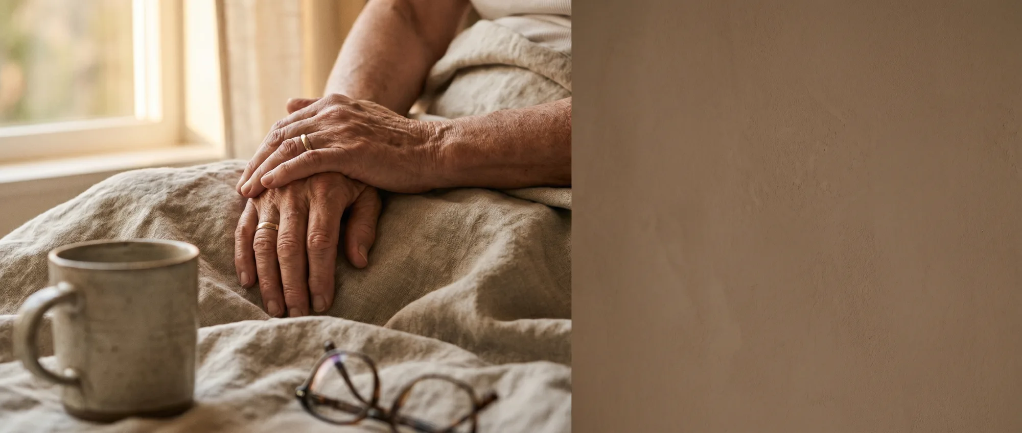 Two hands resting gently together on warm linen in soft morning light